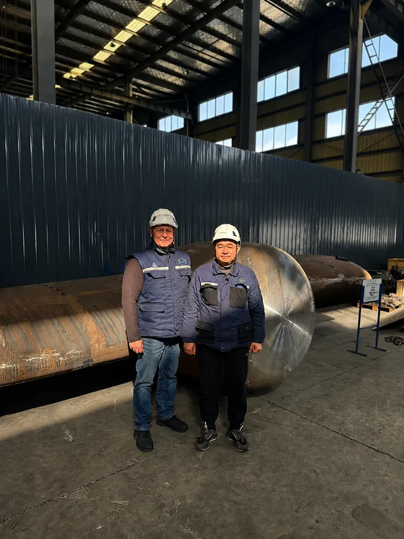 Two employees in front of a rudder stock in the production hall
